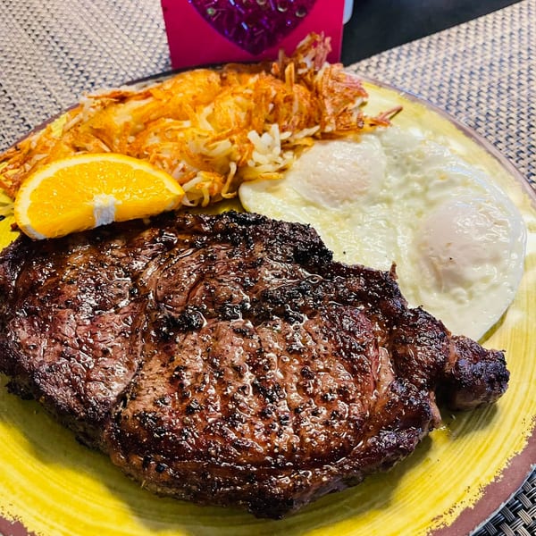 A grilled steak, hash browns, two fried eggs, and an orange slice on a yellow plate.