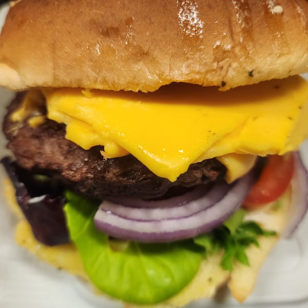 Close-up of a cheeseburger with melted cheese, red onion, lettuce, and tomato on a bun.