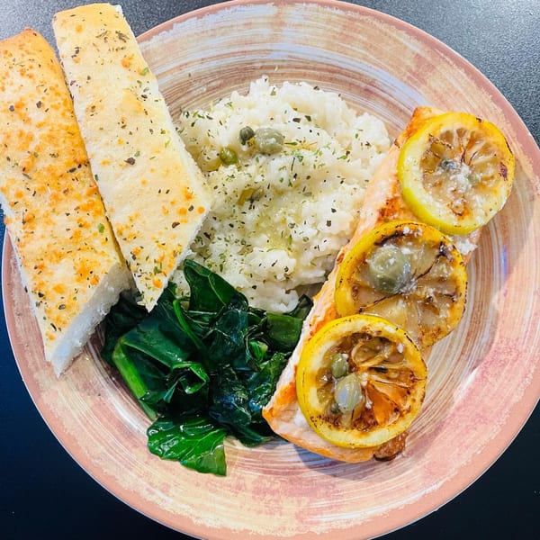 Viney's Italian Kitchen salmon entree with grilled lemon, capers, risotto, sautéed greens, and garlic bread.