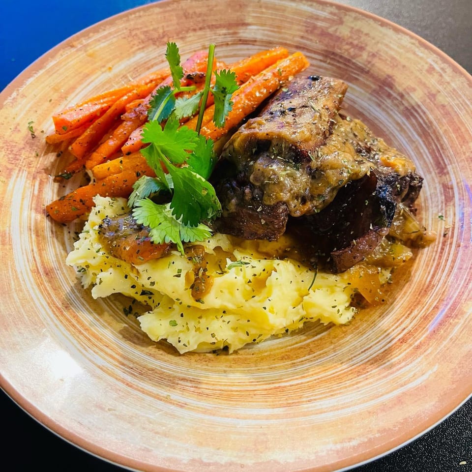 Braised short ribs with mashed potatoes, glazed carrots, and fresh herbs on a rustic plate.