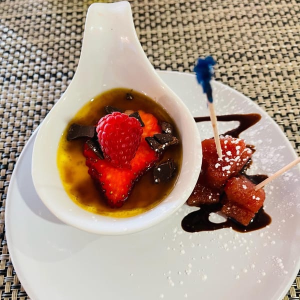 Dessert with strawberries, raspberries, and chocolate in a white dish, alongside fruit skewers.