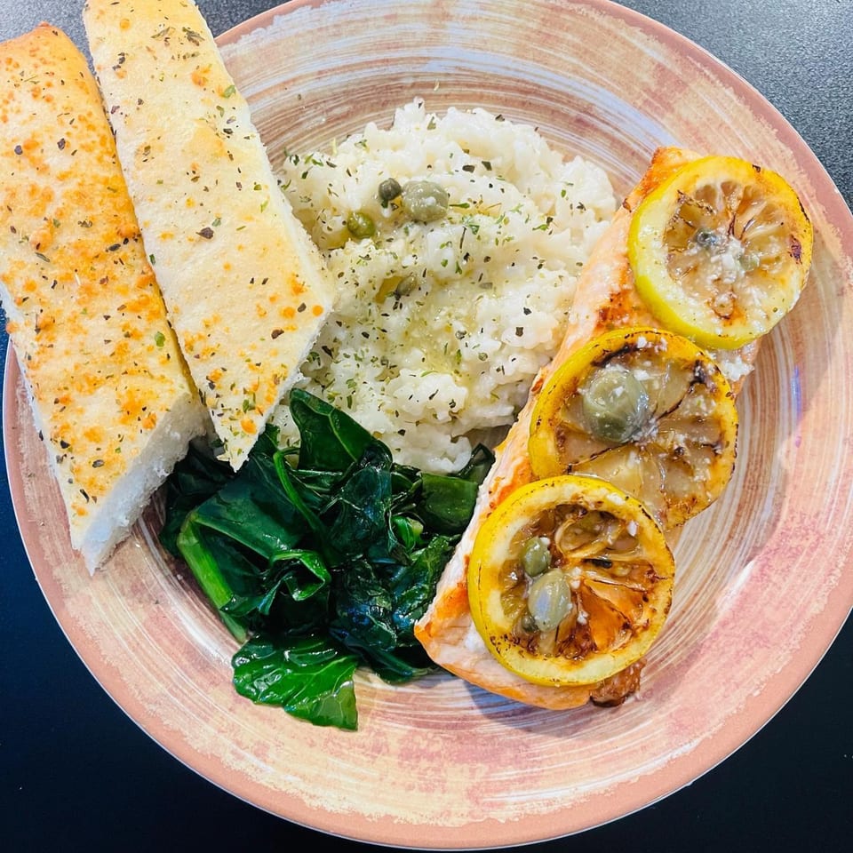 Viney's Italian Kitchen's salmon with lemon, capers, rice, sautéed greens, and two breadsticks.