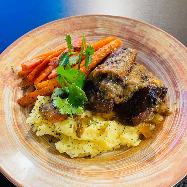 Braised short ribs with mashed potatoes, roasted carrots, and fresh herbs on a rustic plate.